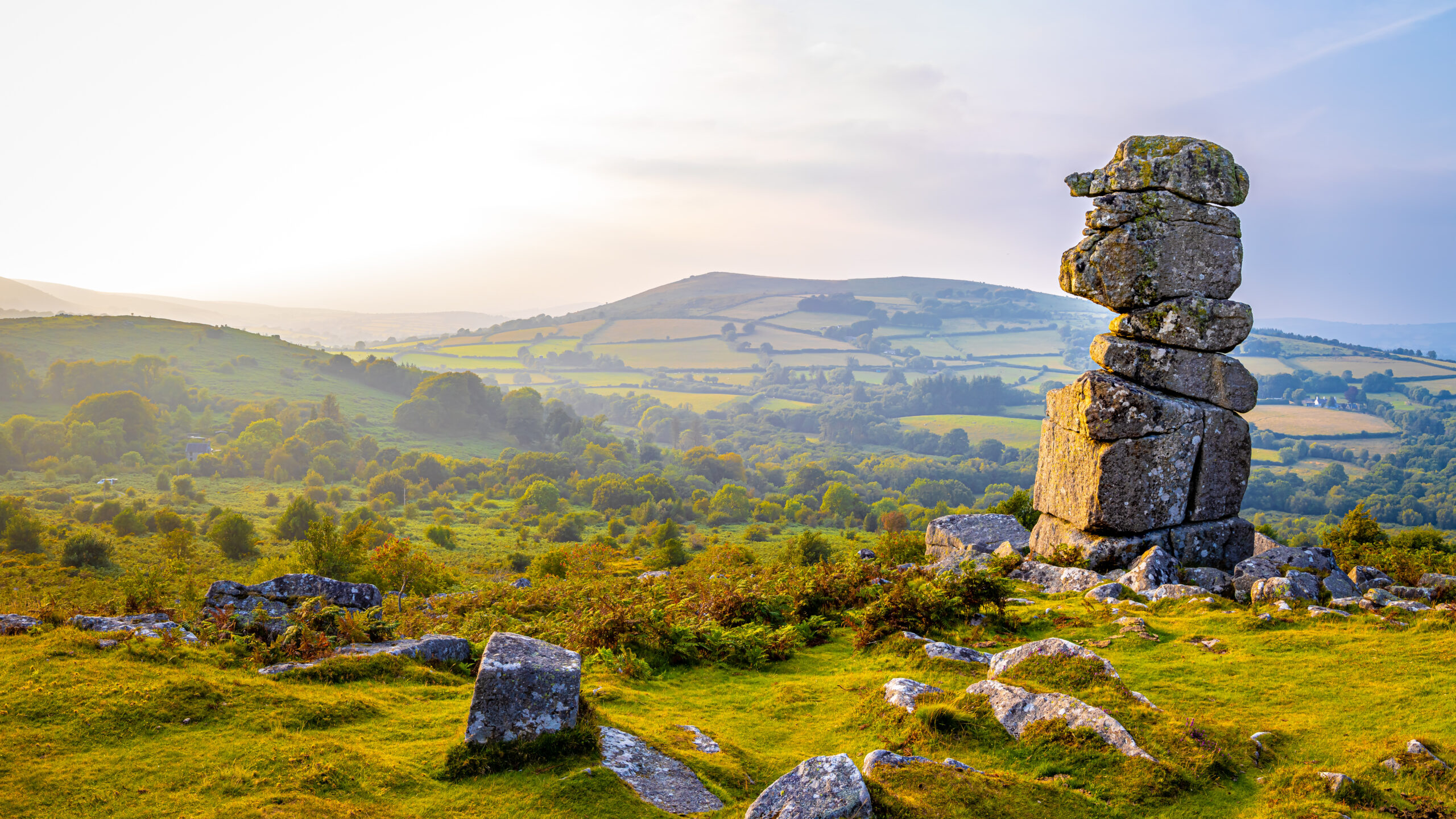 A view of Bowerman's nose, a stone tower overlooking green trees and hills in Dartmoor National Park