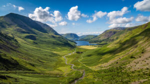 View of Warnscale Bottom at the Lake District. A valley between to large hilly landscapes of green and a lake in the far distance on a sunny day.